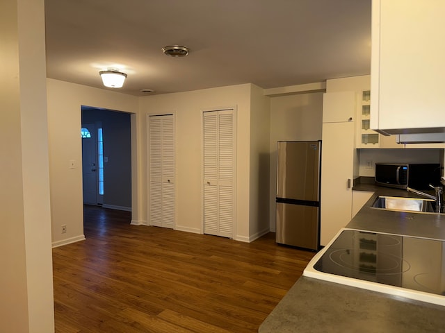 kitchen with stainless steel appliances, a sink, white cabinetry, baseboards, and dark wood finished floors