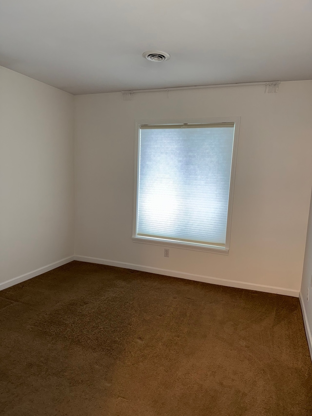 spare room with dark colored carpet, visible vents, and baseboards