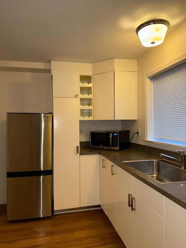 kitchen with stainless steel appliances, dark countertops, white cabinets, and a sink