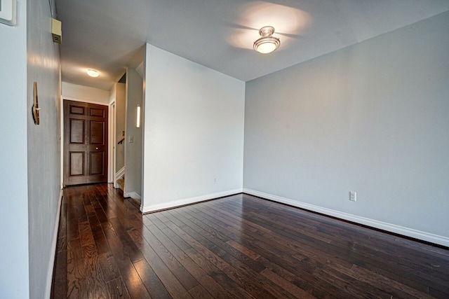 empty room with stairs, dark wood-type flooring, and baseboards