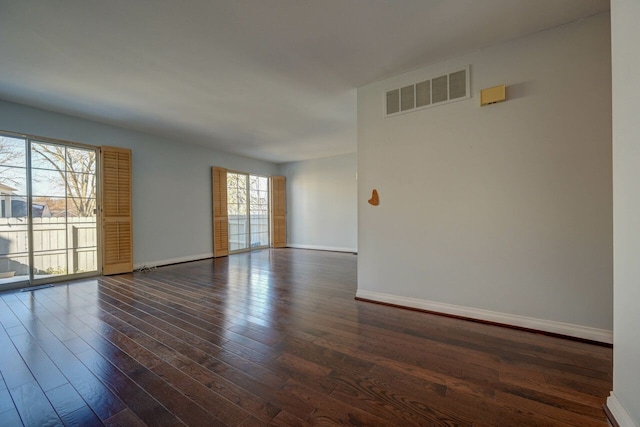 spare room featuring dark wood-style floors, visible vents, and baseboards