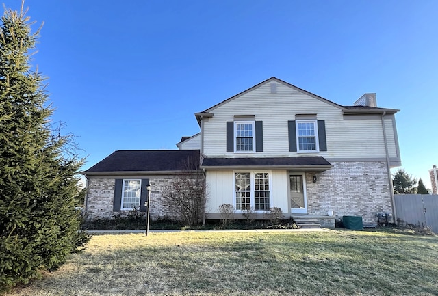 traditional home featuring brick siding, a chimney, a front lawn, and fence