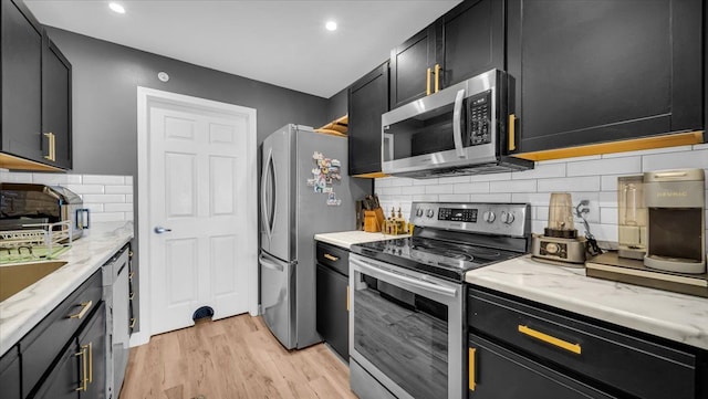 kitchen with light wood-type flooring, light stone countertops, stainless steel appliances, and decorative backsplash