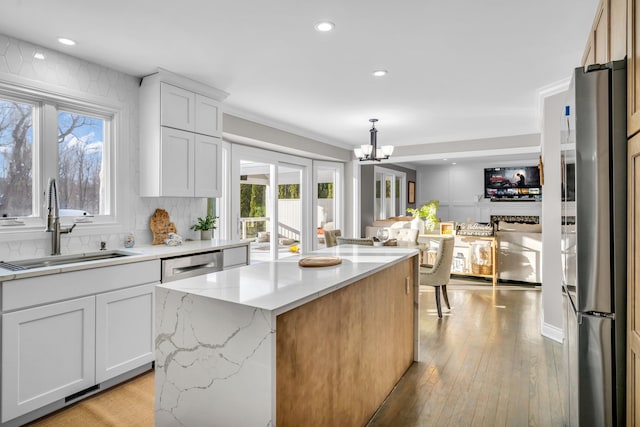 kitchen featuring stainless steel appliances, a sink, a kitchen island, white cabinets, and pendant lighting