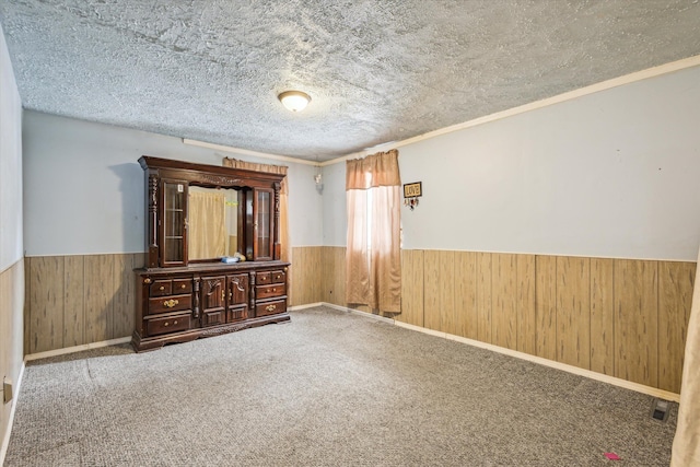 spare room featuring ornamental molding, carpet floors, a textured ceiling, and wooden walls