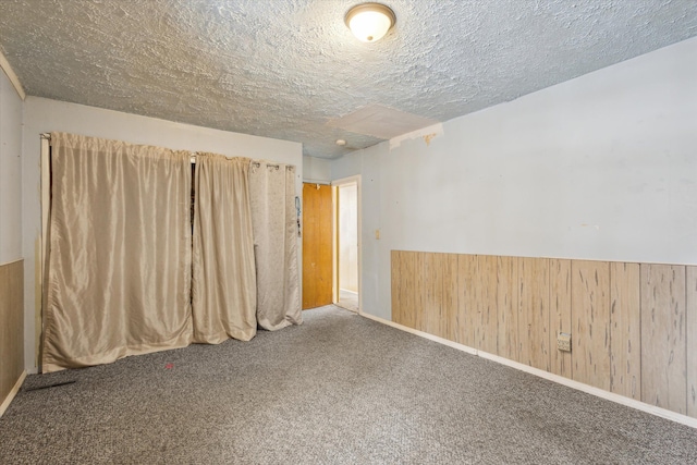 empty room featuring carpet, wooden walls, and a textured ceiling