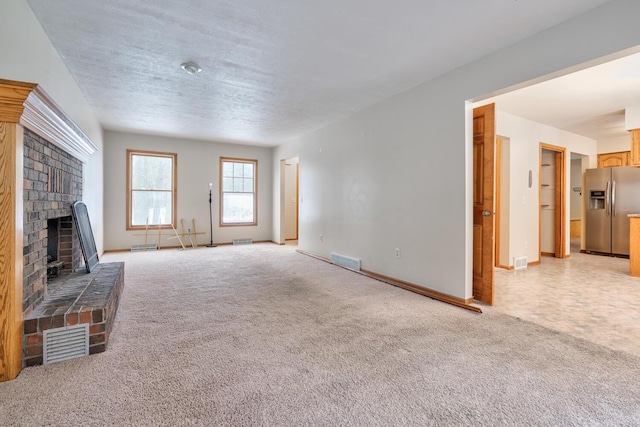 unfurnished living room with light colored carpet, a brick fireplace, and a textured ceiling