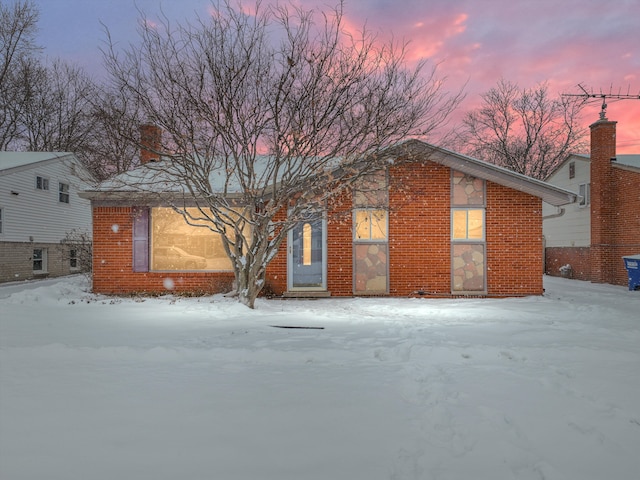 snow covered back of property featuring brick siding