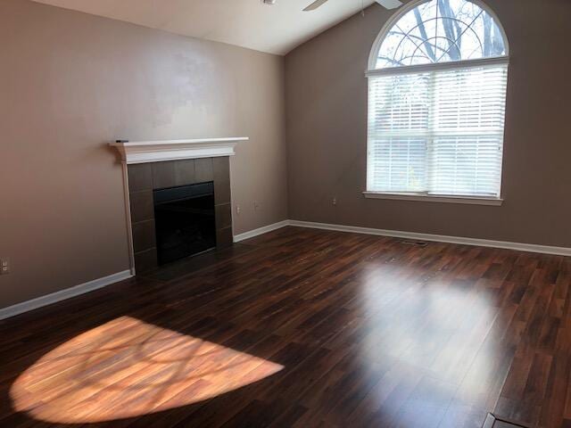 unfurnished living room featuring a tiled fireplace, lofted ceiling, dark hardwood / wood-style floors, and ceiling fan