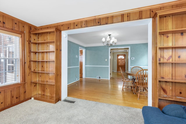 interior space with wood walls, light carpet, ornamental molding, an inviting chandelier, and built in features