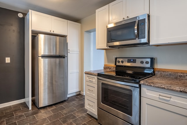 kitchen featuring appliances with stainless steel finishes, dark countertops, white cabinets, and baseboards