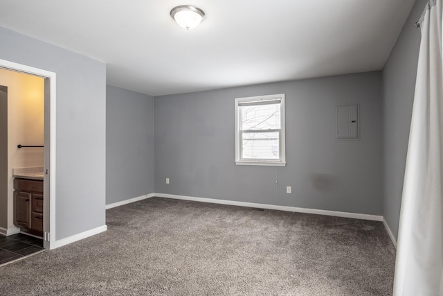 unfurnished bedroom featuring electric panel, dark carpet, ensuite bath, and baseboards