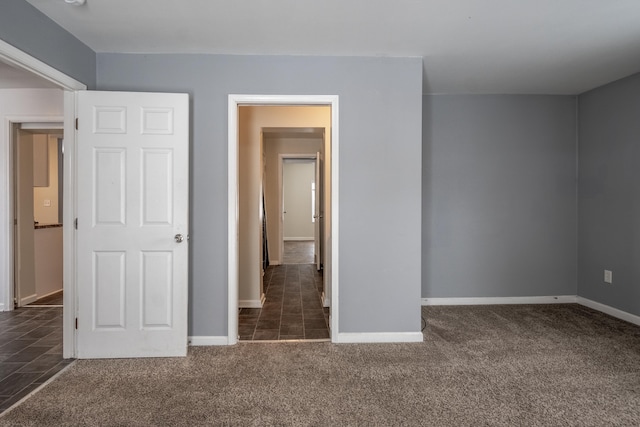 unfurnished bedroom with dark carpet and baseboards