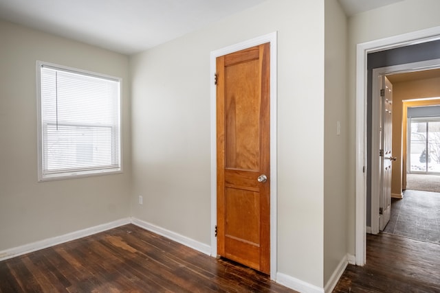 spare room with baseboards and dark wood-type flooring