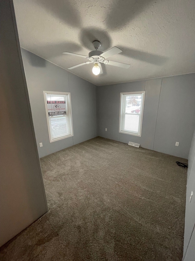 unfurnished room featuring ceiling fan, vaulted ceiling, carpet floors, and a textured ceiling