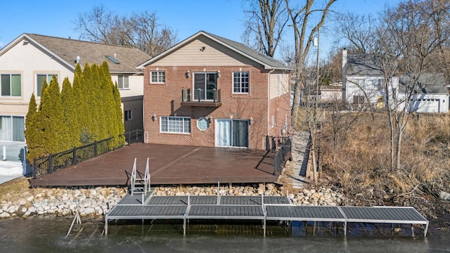 back of property with a wooden deck, brick siding, and a balcony