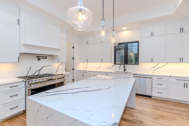 kitchen featuring stainless steel appliances, a tray ceiling, light stone countertops, white cabinets, and decorative light fixtures