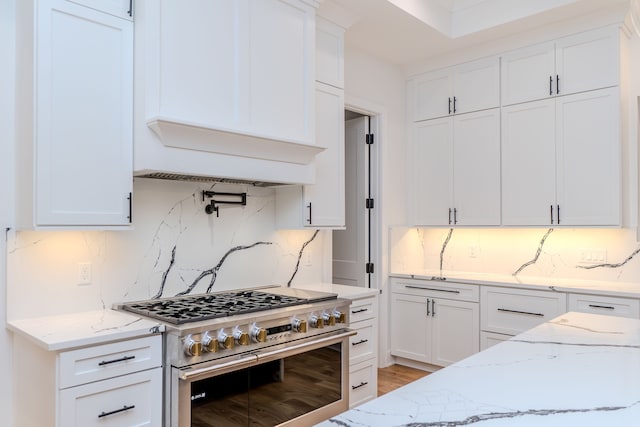 kitchen with white cabinetry, light stone counters, and range with two ovens