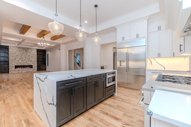 kitchen with decorative light fixtures, white cabinets, built in appliances, light hardwood / wood-style floors, and light stone countertops