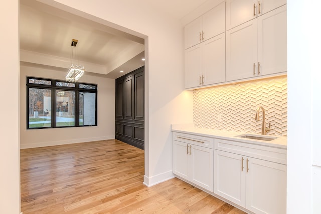 kitchen featuring decorative light fixtures, sink, white cabinets, decorative backsplash, and a raised ceiling