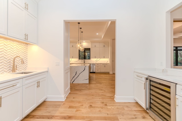 kitchen featuring sink, hanging light fixtures, beverage cooler, and white cabinets