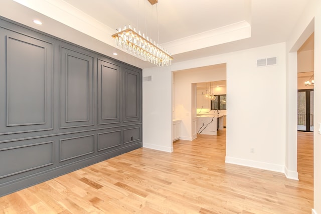 unfurnished dining area with a tray ceiling, a chandelier, and light hardwood / wood-style floors