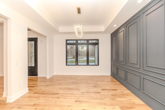 unfurnished room featuring an inviting chandelier, a tray ceiling, and light wood-type flooring