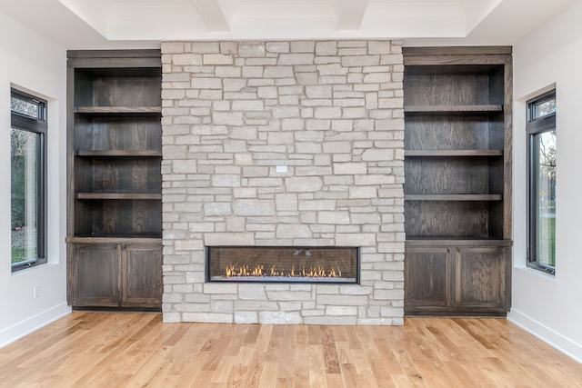 unfurnished living room with a stone fireplace, light wood-type flooring, and built in shelves