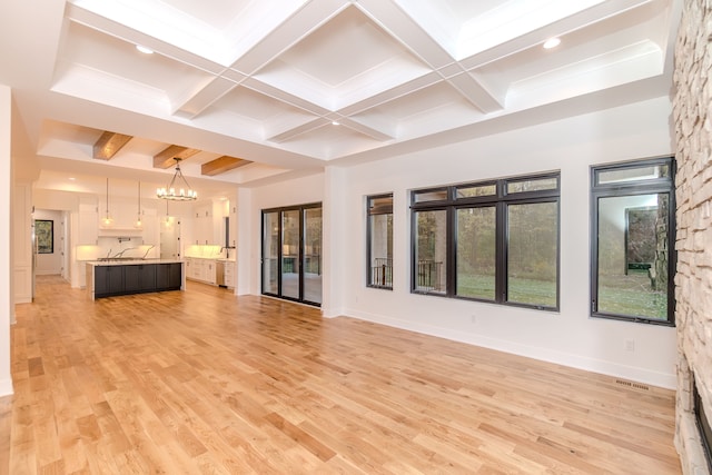 unfurnished living room featuring coffered ceiling, beam ceiling, light wood-type flooring, and a notable chandelier