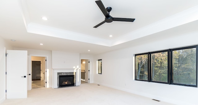 unfurnished living room with ceiling fan, light colored carpet, a fireplace, and a raised ceiling