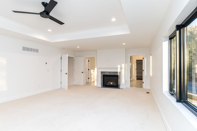 unfurnished living room featuring light colored carpet, a premium fireplace, and a tray ceiling