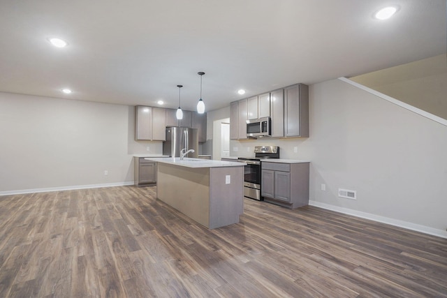 kitchen with pendant lighting, gray cabinets, appliances with stainless steel finishes, dark hardwood / wood-style floors, and an island with sink