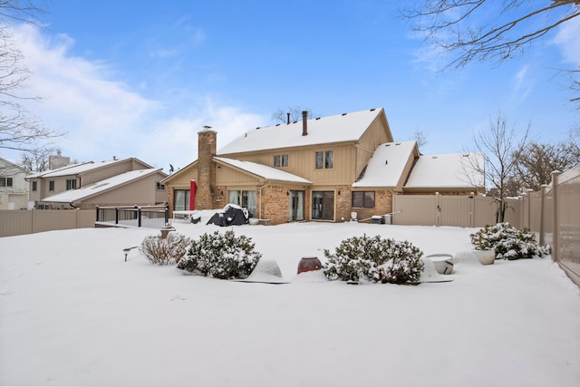 snow covered house with brick siding and fence