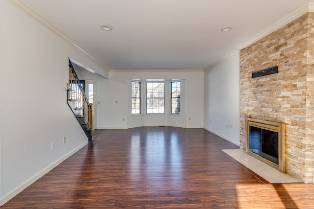 unfurnished living room featuring a stone fireplace, baseboards, stairs, dark wood finished floors, and crown molding