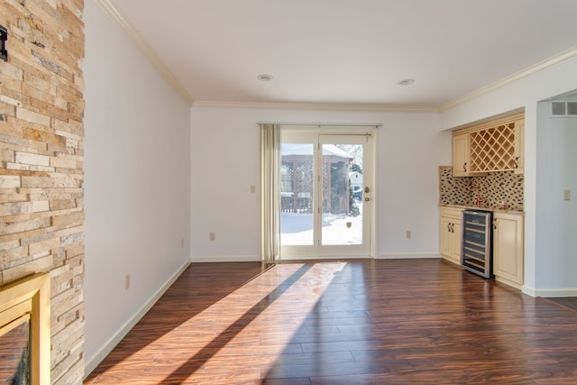 unfurnished living room with wine cooler, dark wood-type flooring, baseboards, a bar, and crown molding