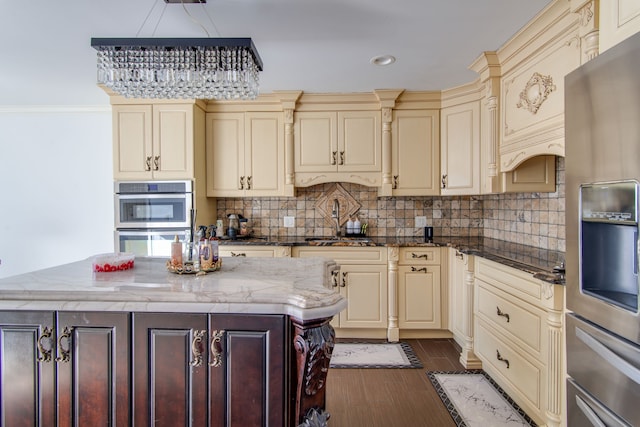 kitchen featuring stainless steel appliances, cream cabinetry, backsplash, a center island, and dark stone counters