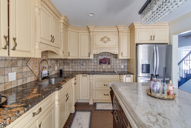 kitchen with dark stone counters, a sink, stainless steel refrigerator with ice dispenser, and cream cabinets