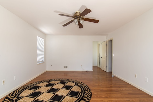 spare room with a ceiling fan, visible vents, baseboards, and wood finished floors