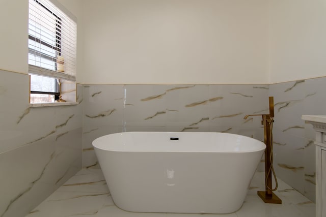 full bath with marble finish floor, a wainscoted wall, and a freestanding tub