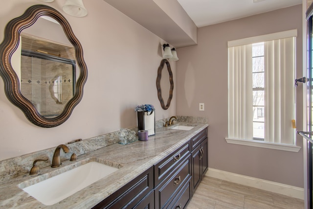 full bath featuring an enclosed shower, a sink, baseboards, and double vanity