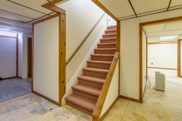 stairs with a paneled ceiling, baseboards, and unfinished concrete flooring