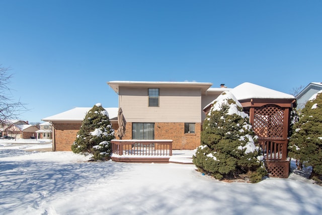 snow covered house with a deck and brick siding