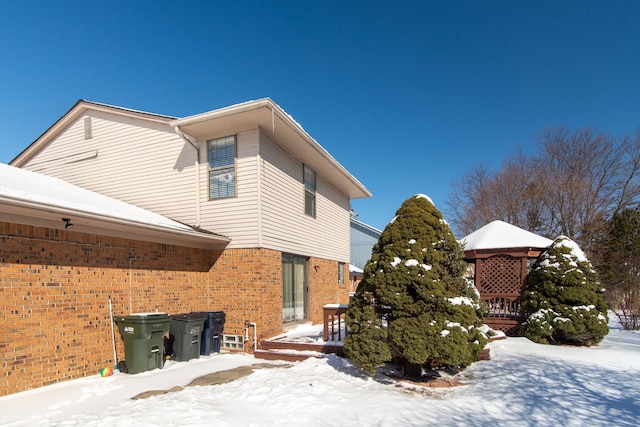 view of snowy exterior with brick siding and a gazebo