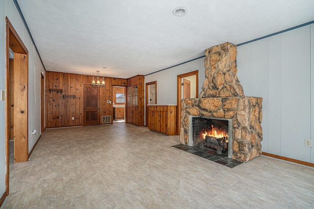 unfurnished living room with a stone fireplace, an inviting chandelier, and wood walls