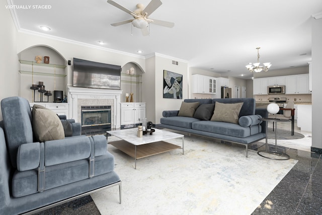 living room with crown molding, a tiled fireplace, and ceiling fan with notable chandelier