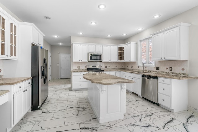 kitchen featuring sink, backsplash, stainless steel appliances, white cabinets, and a kitchen island