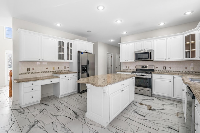 kitchen featuring white cabinets, decorative backsplash, a center island, light stone counters, and stainless steel appliances