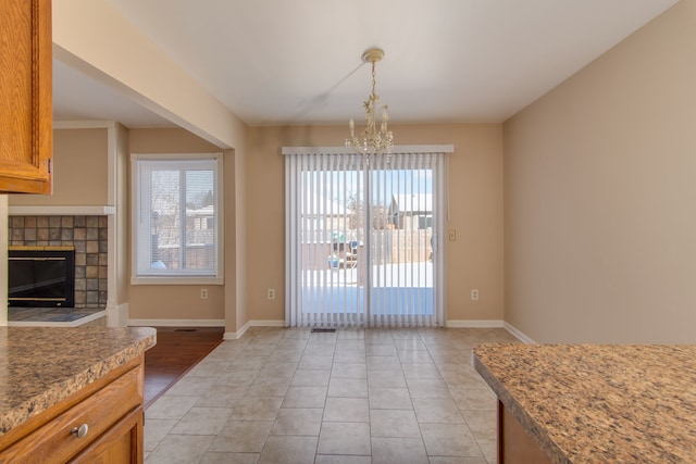 dining space with baseboards, a notable chandelier, a tiled fireplace, and light tile patterned floors