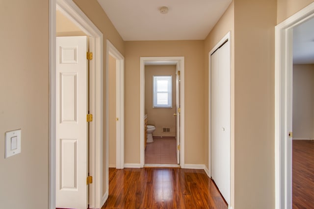 corridor featuring dark wood-style flooring, visible vents, and baseboards