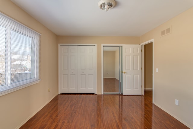 unfurnished bedroom featuring two closets, baseboards, visible vents, and dark wood-style flooring